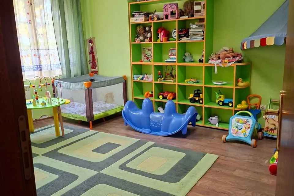 Занималнята, погледната от вратата: кошара, кръгла масичка и синя клатушка